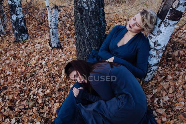 Портрет двух женщин, сидящих в лесу и прислонившихся к дереву — стоковое фото