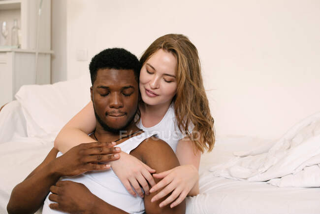 Retrato de um casal misto sentado na sala de estar abraçando — Fotografia de Stock
