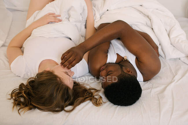 Coppie di razza mista sdraiato a letto guardando l'un l'altro — Foto stock