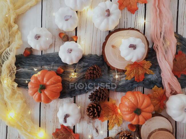 Citrouille, cône de pin, feuilles d'automne et présentoir de lumière de fée sur une table — Photo de stock