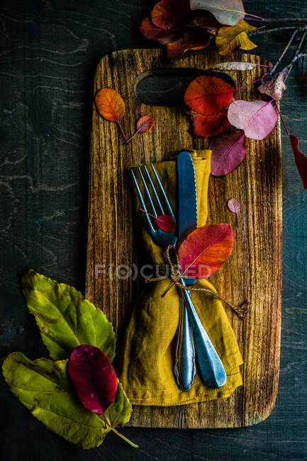 Autumnal place setting on a chopping board with autumn leaves — Stock Photo