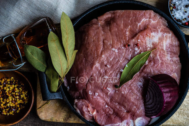Junta de cerdo en una cacerola con cebolla roja, hojas de laurel, chile y sal - foto de stock