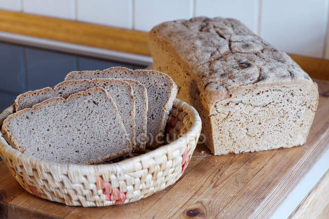 Loaf of home made rye bread and bread basket with slices of bread — Stock Photo