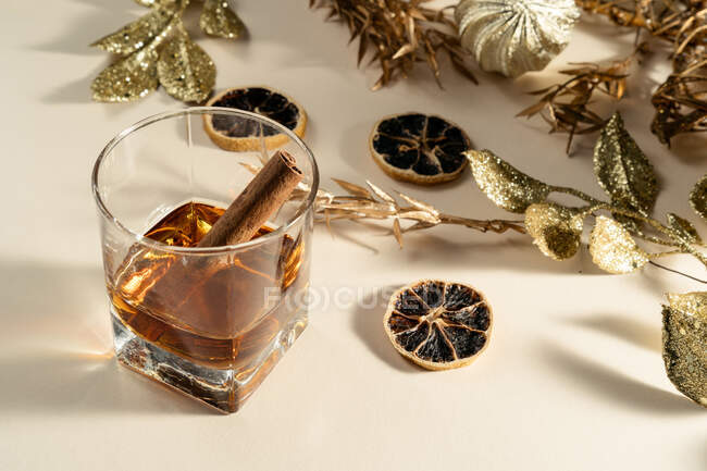 Vaso de whisky con varilla de canela y adornos navideños dorados - foto de stock