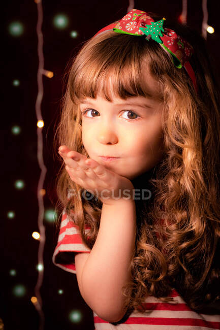 Portrait d'une fille souriante qui souffle des baisers devant les lumières de Noël — Photo de stock
