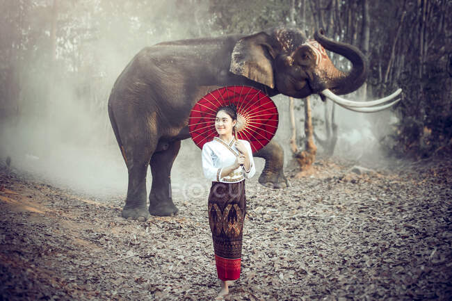 Mulher com um guarda-sol em pé na frente de um elefante, Tailândia — Fotografia de Stock