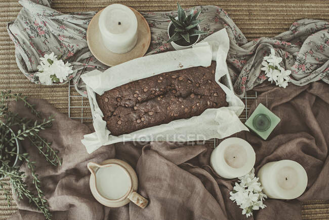 Вид сверху на шоколадный торт со свечами, растениями и горшком сливок — стоковое фото