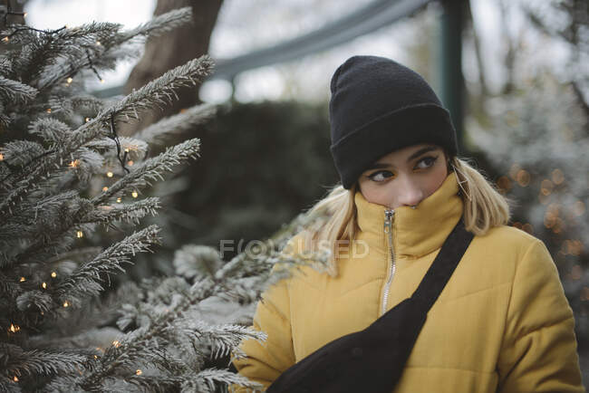 Porträt einer jungen Frau in einer Kugeljacke, die neben einem Weihnachtsbaum steht, Frankreich — Stockfoto