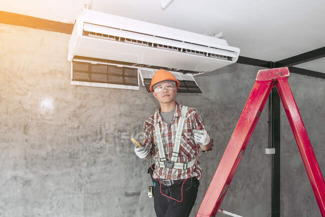 Técnico instalando uma unidade de ar condicionado em uma parede, Tailândia — Fotografia de Stock