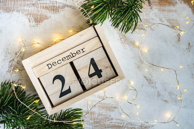 Wooden block calendar for Christmas Eve with fairy lights and fir branches — Stock Photo
