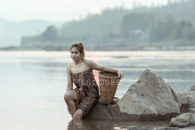 Женщина, сидящая на скале у реки, Таиланд — стоковое фото