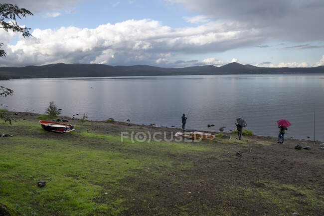 Two people looking at a person fishing in the rain, Lake Bracciano, Lazio, Italy — Stock Photo