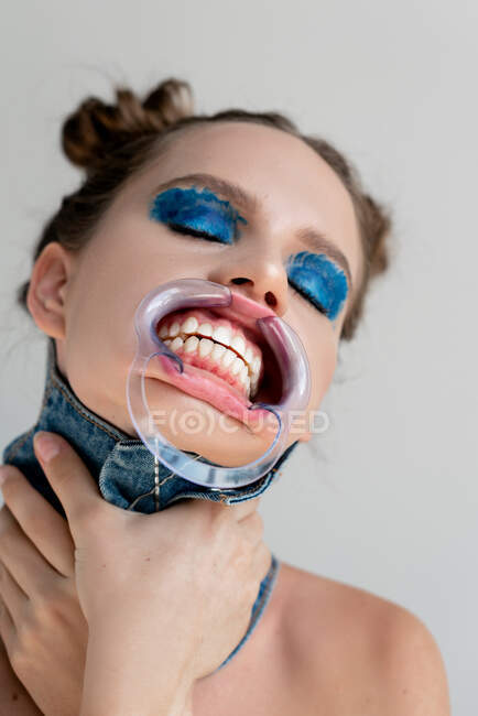 Portrait of a woman wearing a dental mouth retractor choking herself — Stock Photo