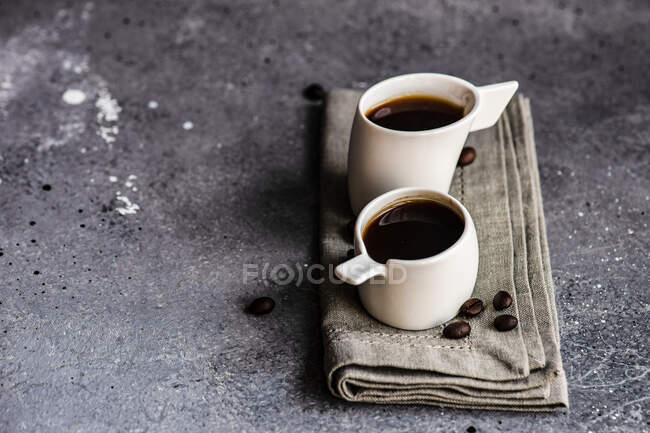 Tazas blancas de cerámica con bebida de café caliente sobre fondo textil gris - foto de stock