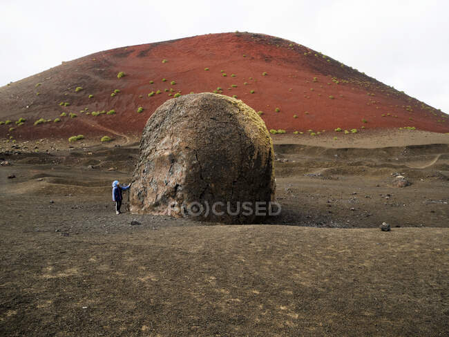 Chica de pie junto a una roca gigante mirando hacia arriba, Lanzarote, Islas Canarias, España - foto de stock