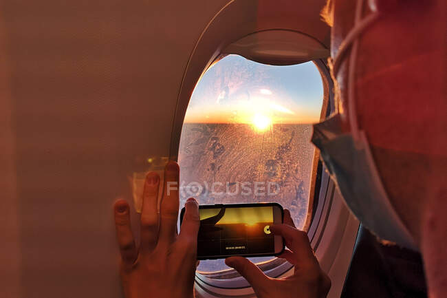 Homme portant un masque facial prenant une photo dans un avion au coucher du soleil — Photo de stock