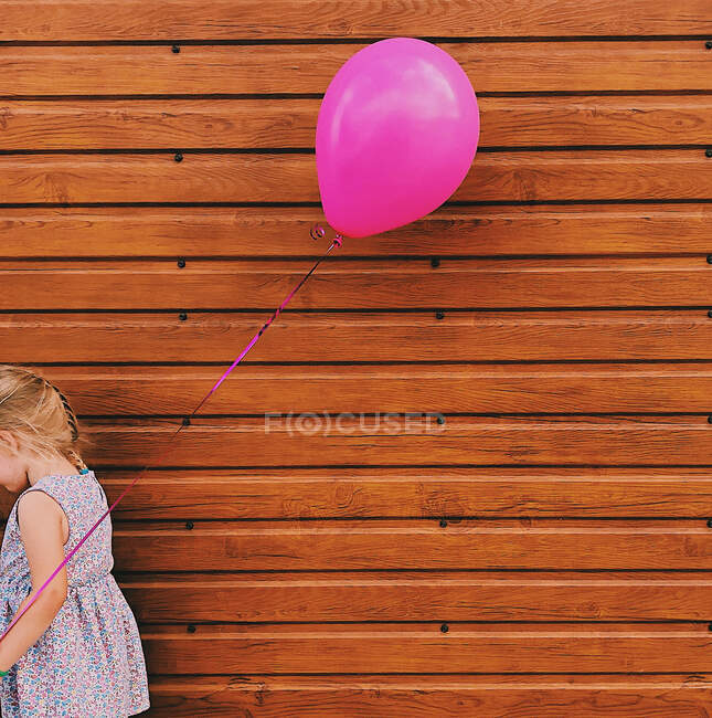 Fille debout près d'un mur en bois tenant un ballon rose — Photo de stock