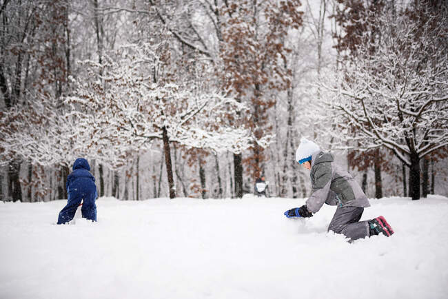 Двое детей катают снег, чтобы сделать снеговика, США — стоковое фото
