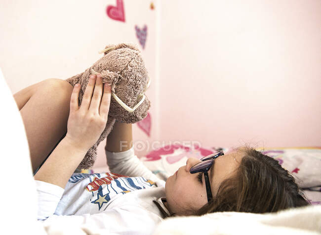 Girl wearing spectacles playing with her teddy bear also wearing spectacles — Stock Photo