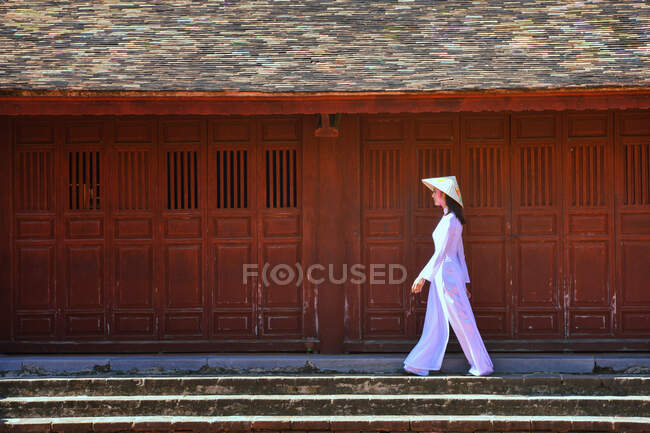 Mujer vestida con Ao dai caminando por un edificio, Hoi an, Vietnam - foto de stock