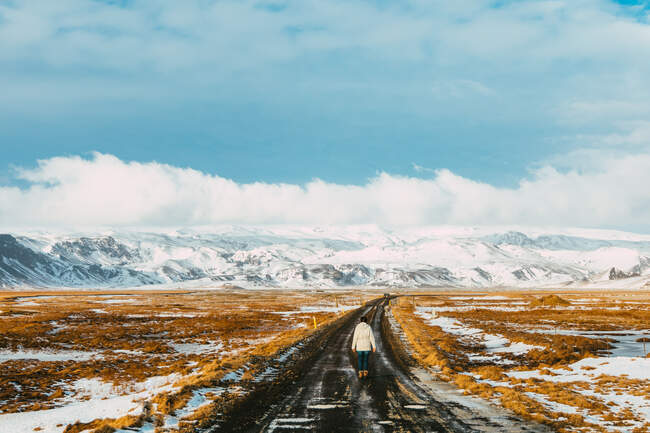 Mulher caminhando ao longo de uma estrada vazia no inverno, Islândia — Fotografia de Stock