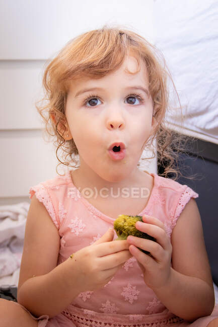 Portrait d'une fille mangeant du brocoli tirant des visages drôles — Photo de stock