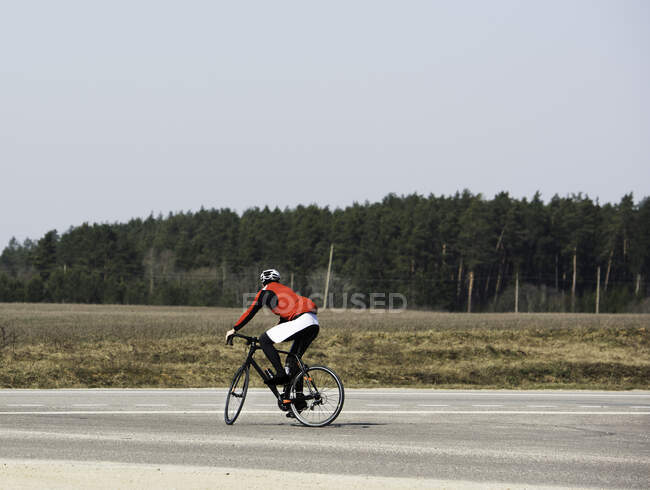 Человек на велосипеде по пустой дороге, Литва — стоковое фото
