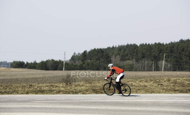 Hombre en bicicleta por un camino vacío, Lituania - foto de stock