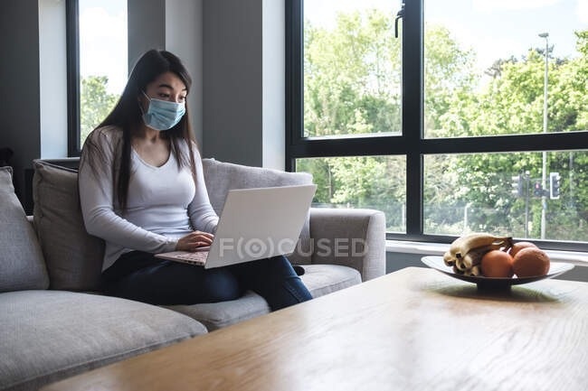 Mulher sentada em um sofá trabalhando em casa durante o confinamento — Fotografia de Stock