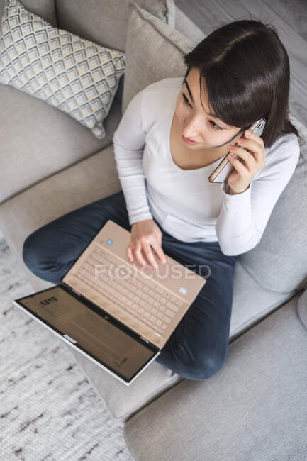 Woman sitting on a sofa working from home - foto de stock