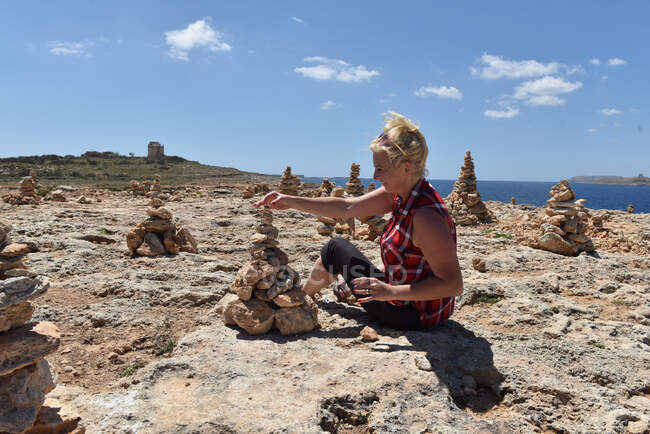 Woman sitting near coast stacking rocks, Coral Beach Bay, Malta — Stock Photo