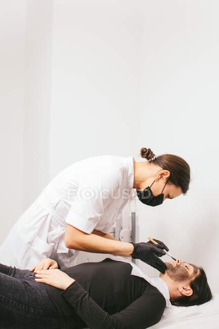 Esteticista preparando a una mujer para un tratamiento de belleza de la cáscara de carbono en una clínica - foto de stock