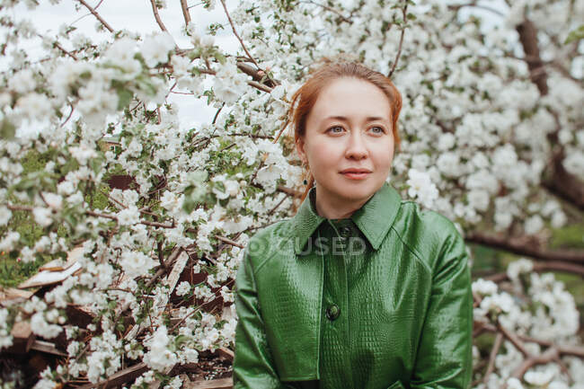 Mulher sorridente em pé ao ar livre por uma árvore de flor de cerejeira — Fotografia de Stock