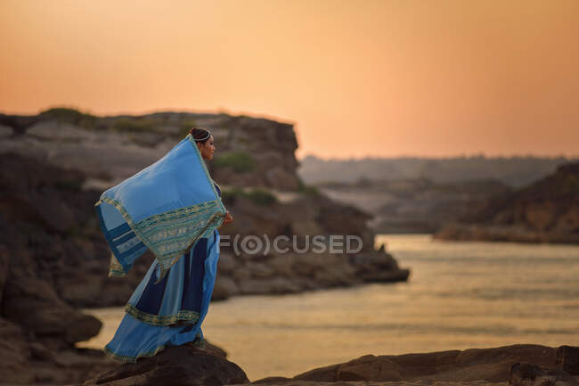 Belle femme portant des vêtements traditionnels du Moyen-Orient debout sur des rochers par la mer — Photo de stock