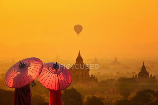 Vista trasera de dos monjes con sombrillas que miran, Bagan, Mandalay, Myanmar - foto de stock