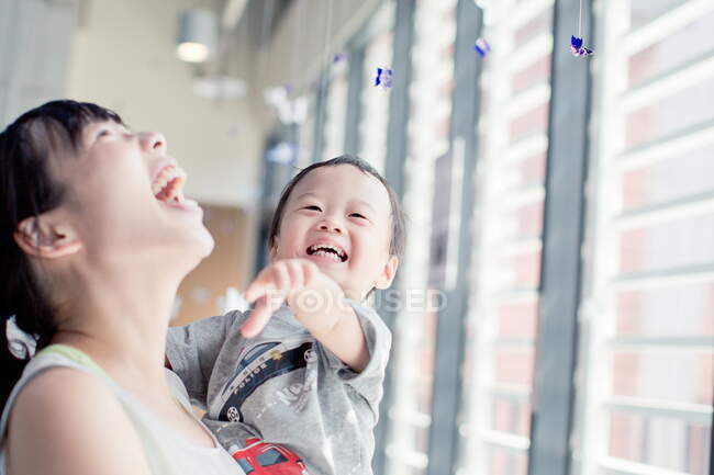 Feliz madre mirando a su hijo jugando con decoraciones de mariposas - foto de stock