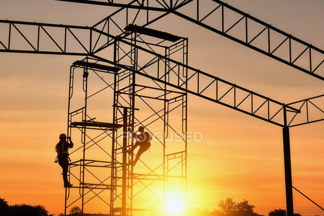Silueta de dos trabajadores de la construcción escalando en andamios, Tailandia - foto de stock