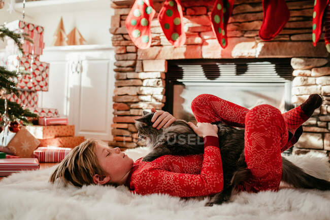 Boy lying on a fluffy rug stroking his cat — Stock Photo