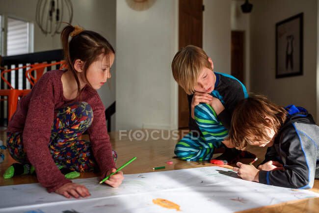 Tres niños pequeños trabajando en un proyecto de arte en casa - foto de stock