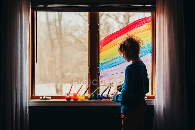 Мальчик рисует радугу на окне, США — стоковое фото