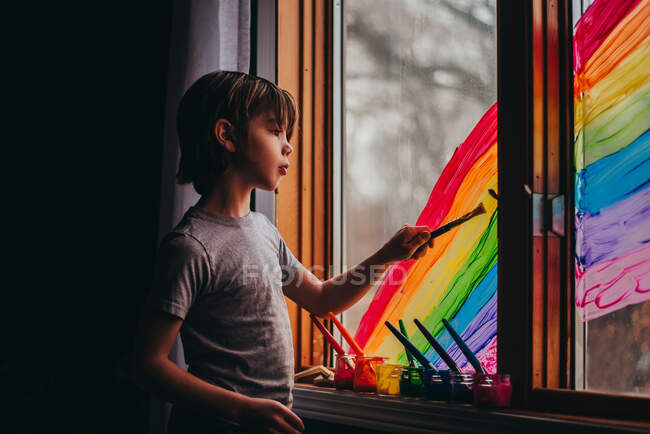 Boy painting a rainbow on a window, USA — Stock Photo