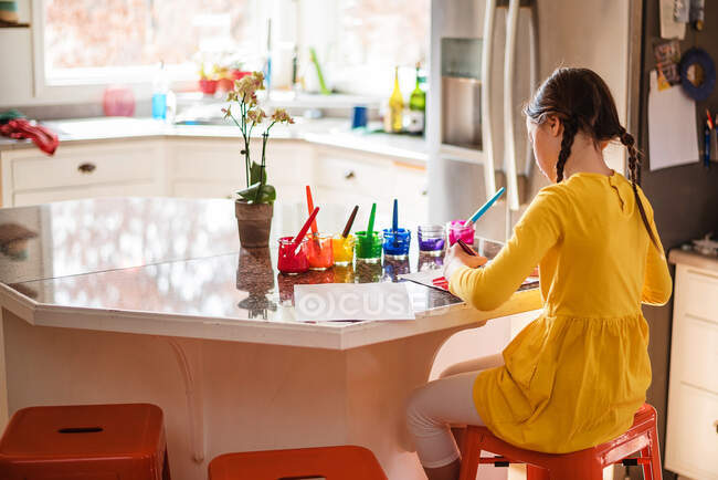 Mädchen sitzt in der Küche und bemalt einen Regenbogen — Stockfoto