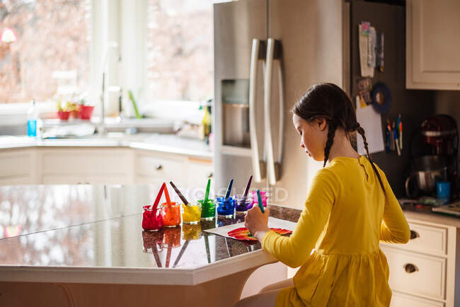 Menina sentada na cozinha pintando um arco-íris — Fotografia de Stock
