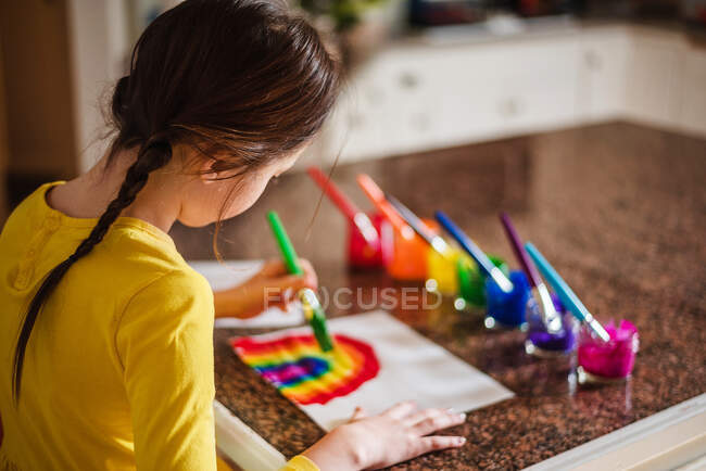 Girl sitting in the kitchen painting a rainbow — Stock Photo