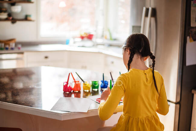 Девушка, сидящая на кухне и рисующая радугу — стоковое фото