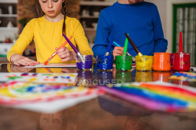 Dos niños sentados en la cocina pintando un arco iris - foto de stock
