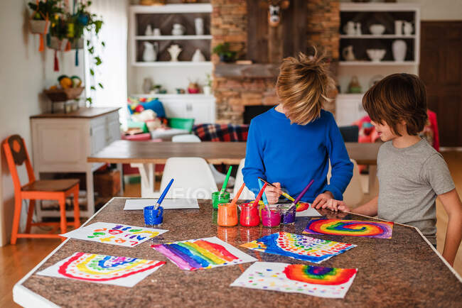 Two boys sitting in the kitchen painting a rainbow — Stock Photo