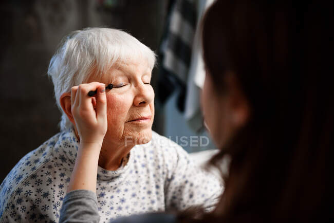 Chica poniendo maquillaje en su abuela - foto de stock