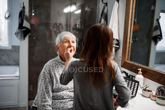 Chica poniendo maquillaje en su abuela - foto de stock