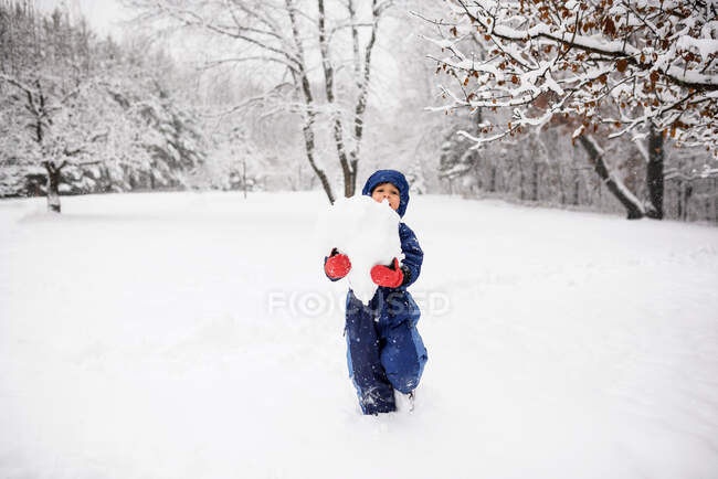 Мальчик, несущий гигантский снежок, чтобы сделать снеговика, США — стоковое фото